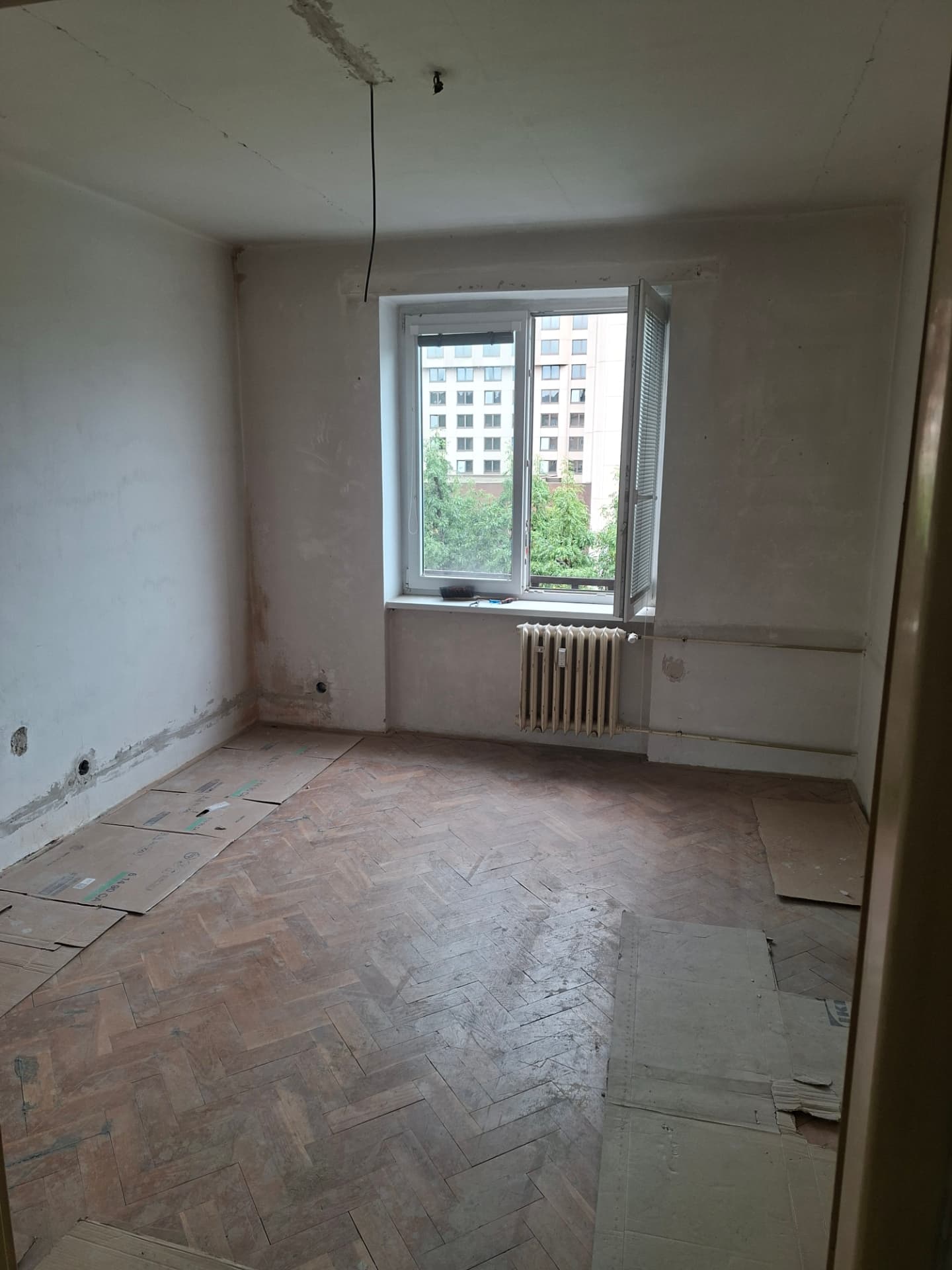Pokoj na Praze 6 před opravou — poškozená omítka u podlahy po elektroinstalaci
