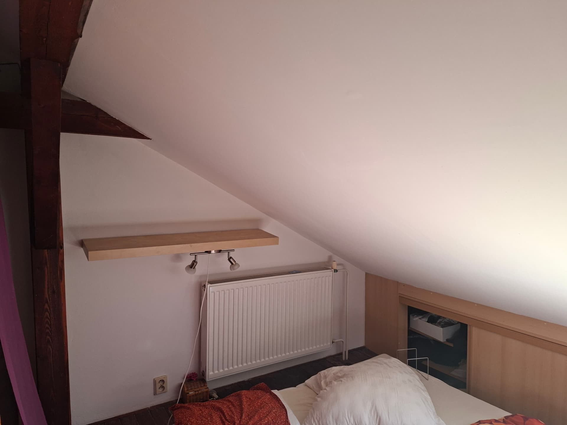 Podkrovní ložnice po výmalbě bílou barvou podél dřevěného trámu